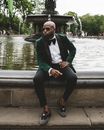 Man in Black Suit Sitting on Concrete Bench Near Body of Water