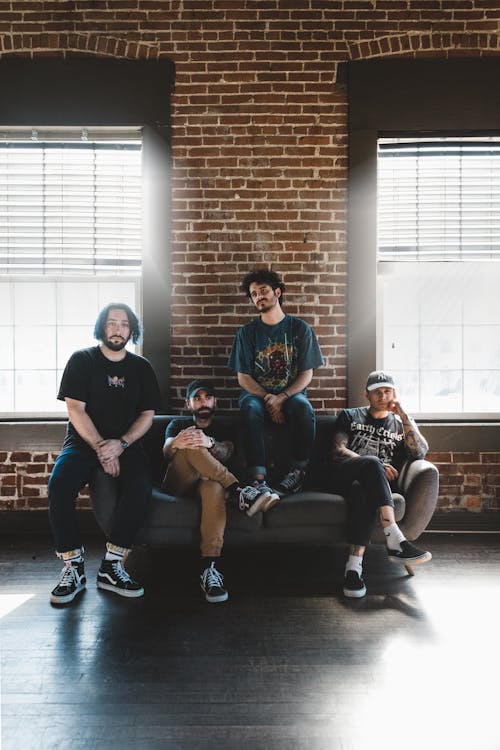 Men Sitting on Gray Sofa beside Brown Brick Wall