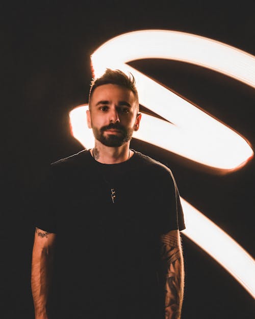 Man in Black Shirt Standing beside Black Wall and White Light