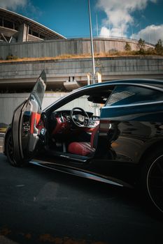 A sleek black luxury sports car with its door open, showcasing a modern urban background.