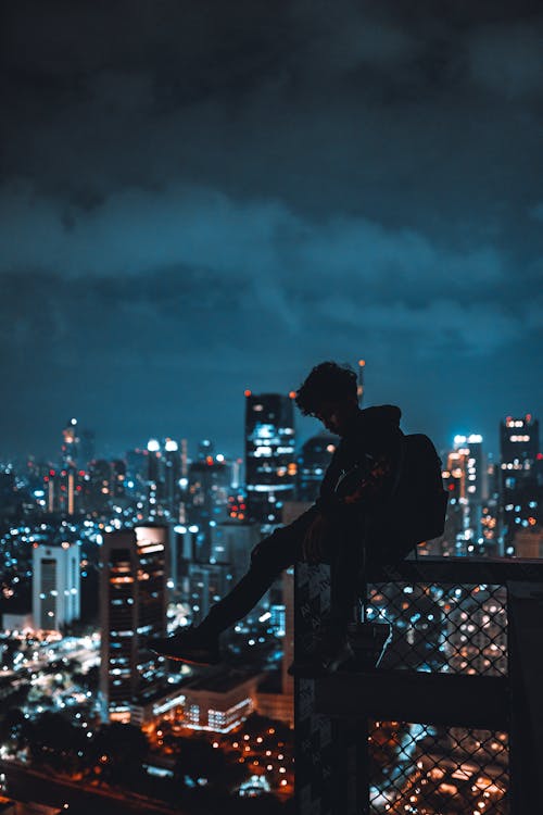 Man Sitting on Railing in City at Night · Free Stock Photo
