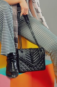 Close-up of a woman sitting with a luxurious black leather handbag and patterned attire.