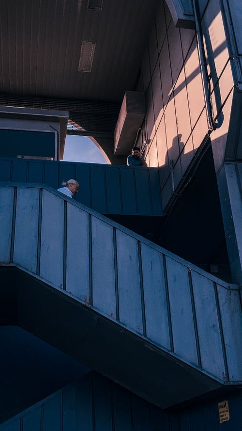 Free A solitary man climbs an industrial staircase in an urban setting during sunset, casting distinct shadows. Stock Photo