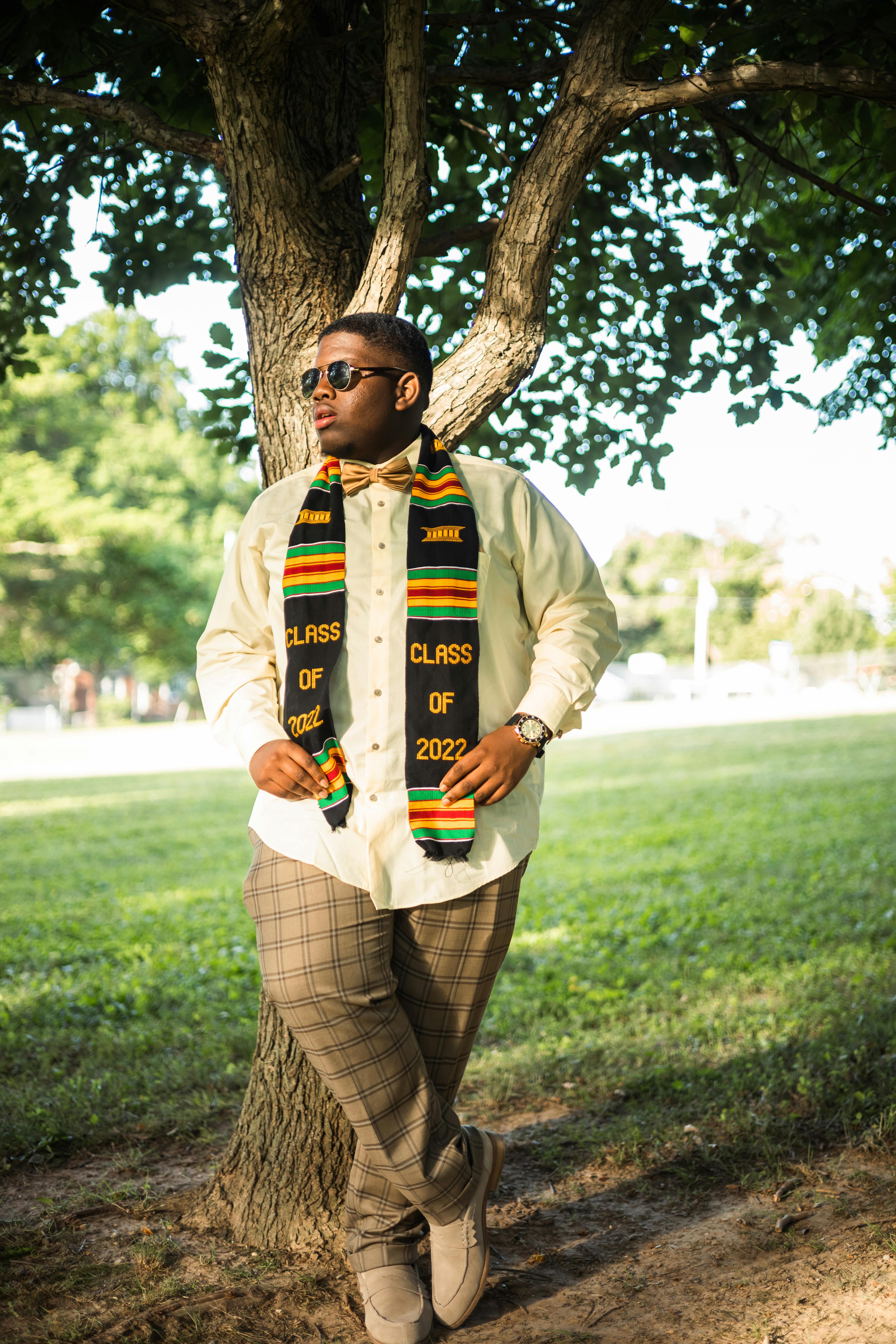 man in yellow long sleeve shirt wearing black and yellow scarf standing beside tree