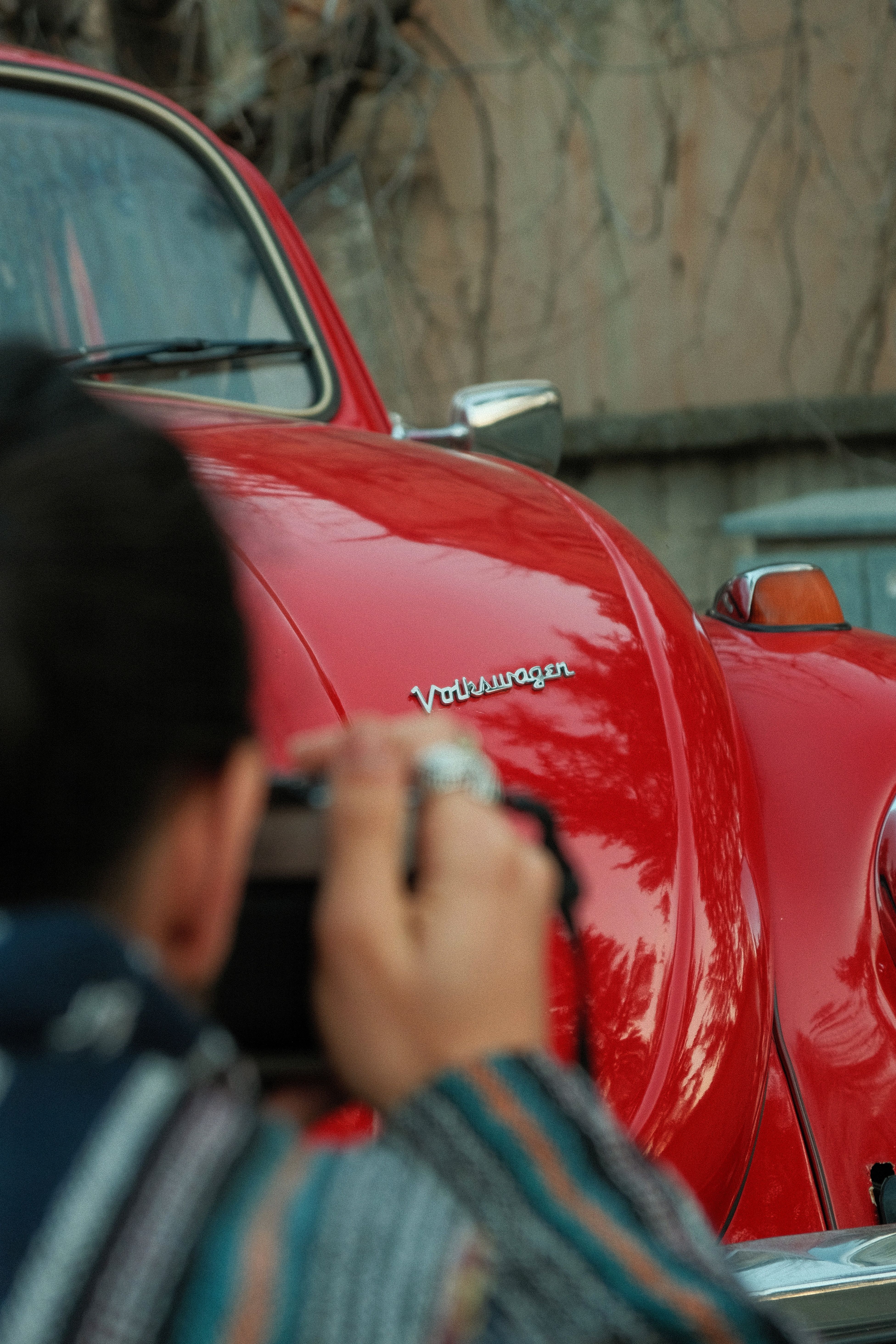 Vintage red Volkswagen Beetle being photographed by a person, emphasizing classic car culture.