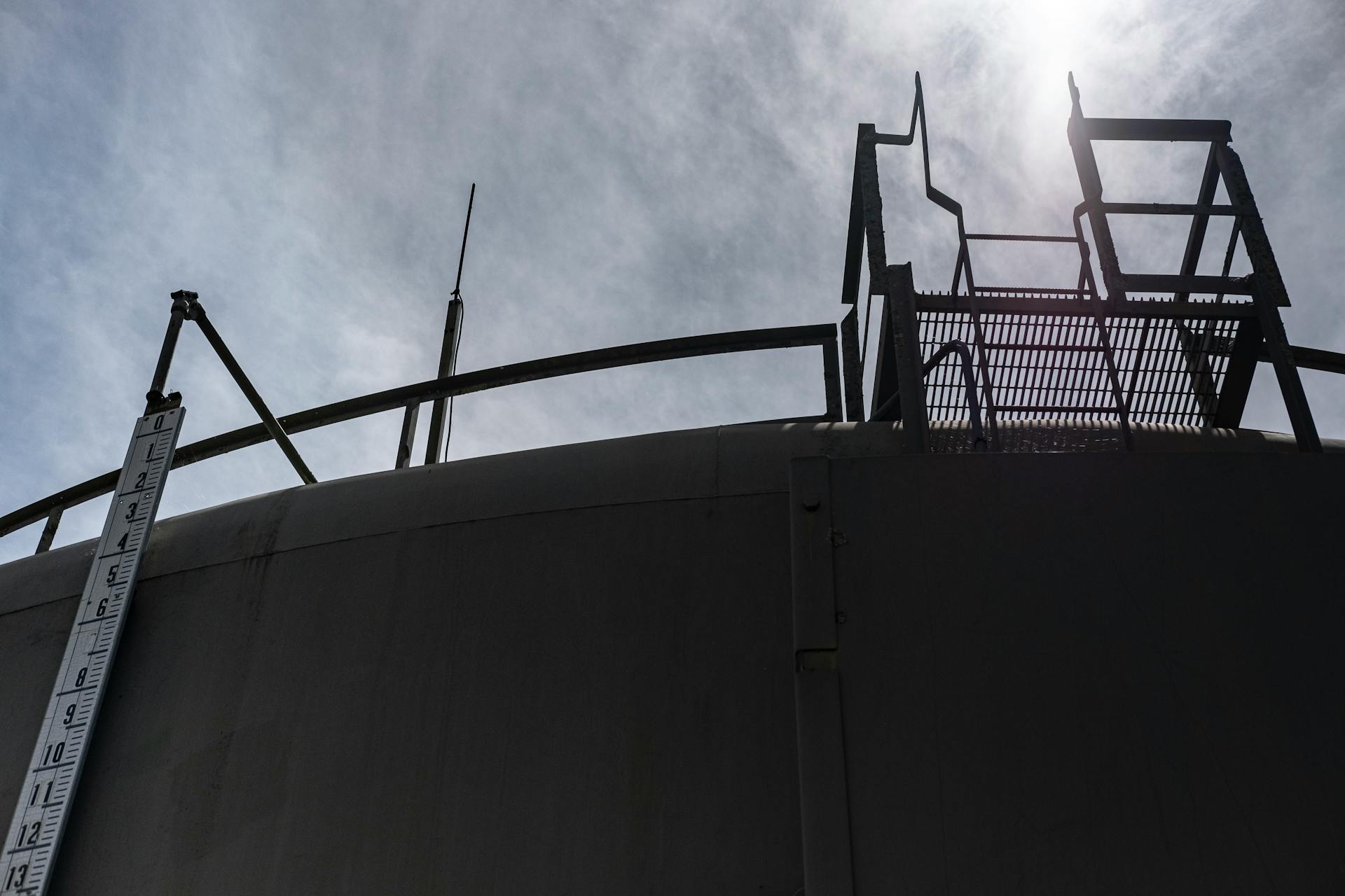 Dramatic low angle shot of a storage tank and metal ladder against a bright sky.