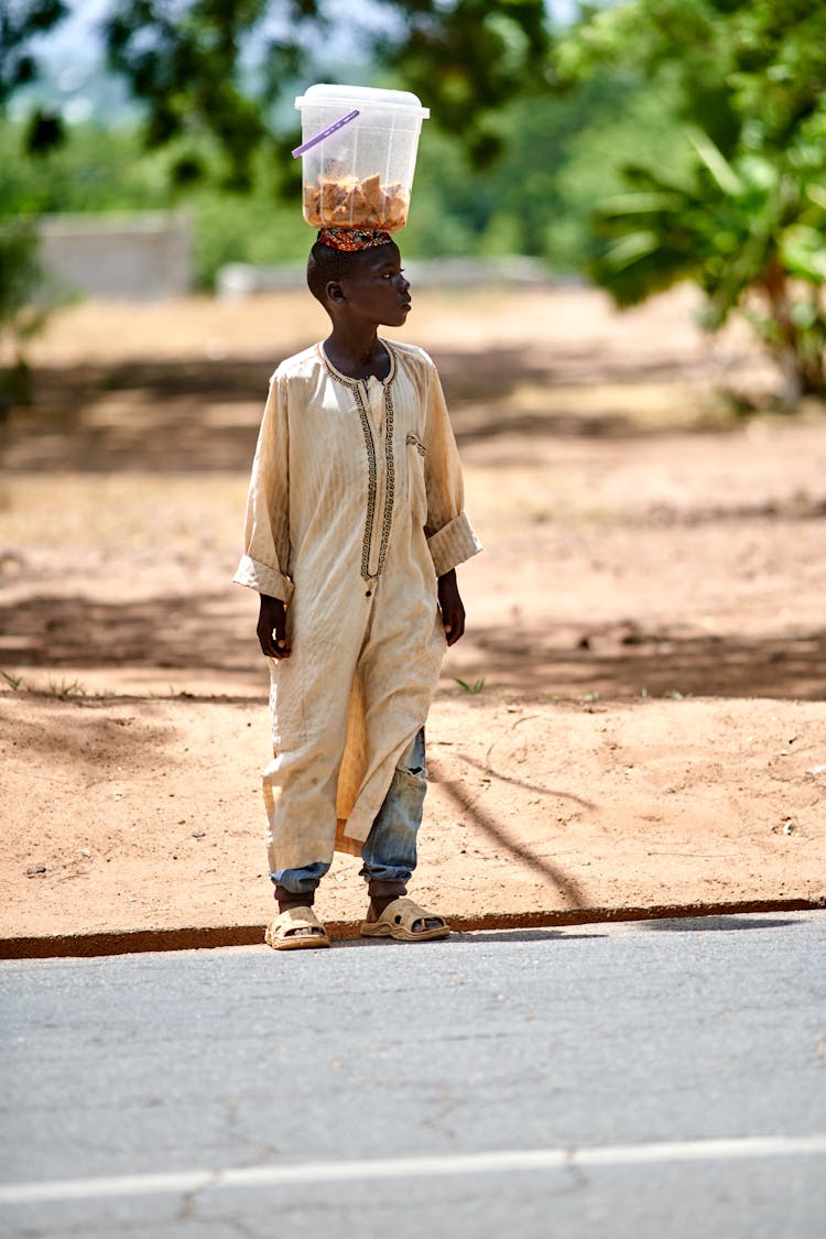 African Boy With Food Container On His Head Standing On The Road