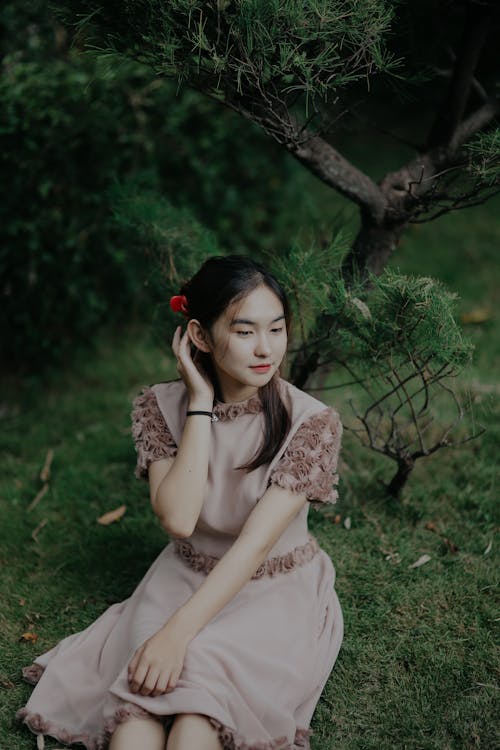 Free Nice Asian Girl Sitting on Grass and Correcting Long Black Hair Stock Photo