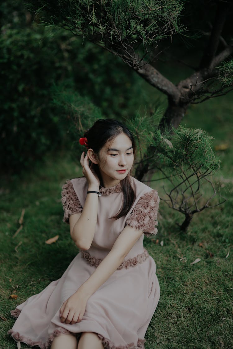 Nice Asian Girl Sitting On Grass And Correcting Long Black Hair