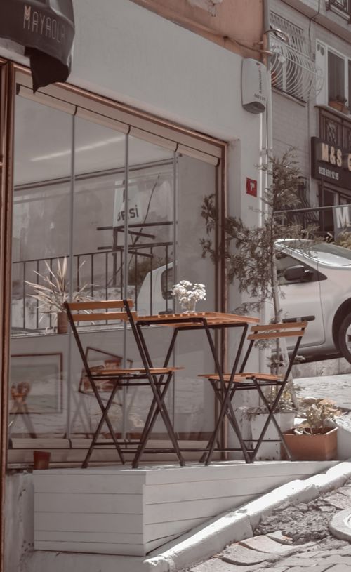 Free A quiet outdoor café setting with wooden chairs and table on a charming street corner, perfect for relaxation. Stock Photo