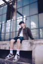 Man in Black Jacket and Blue Shorts Sitting on Concrete Wall