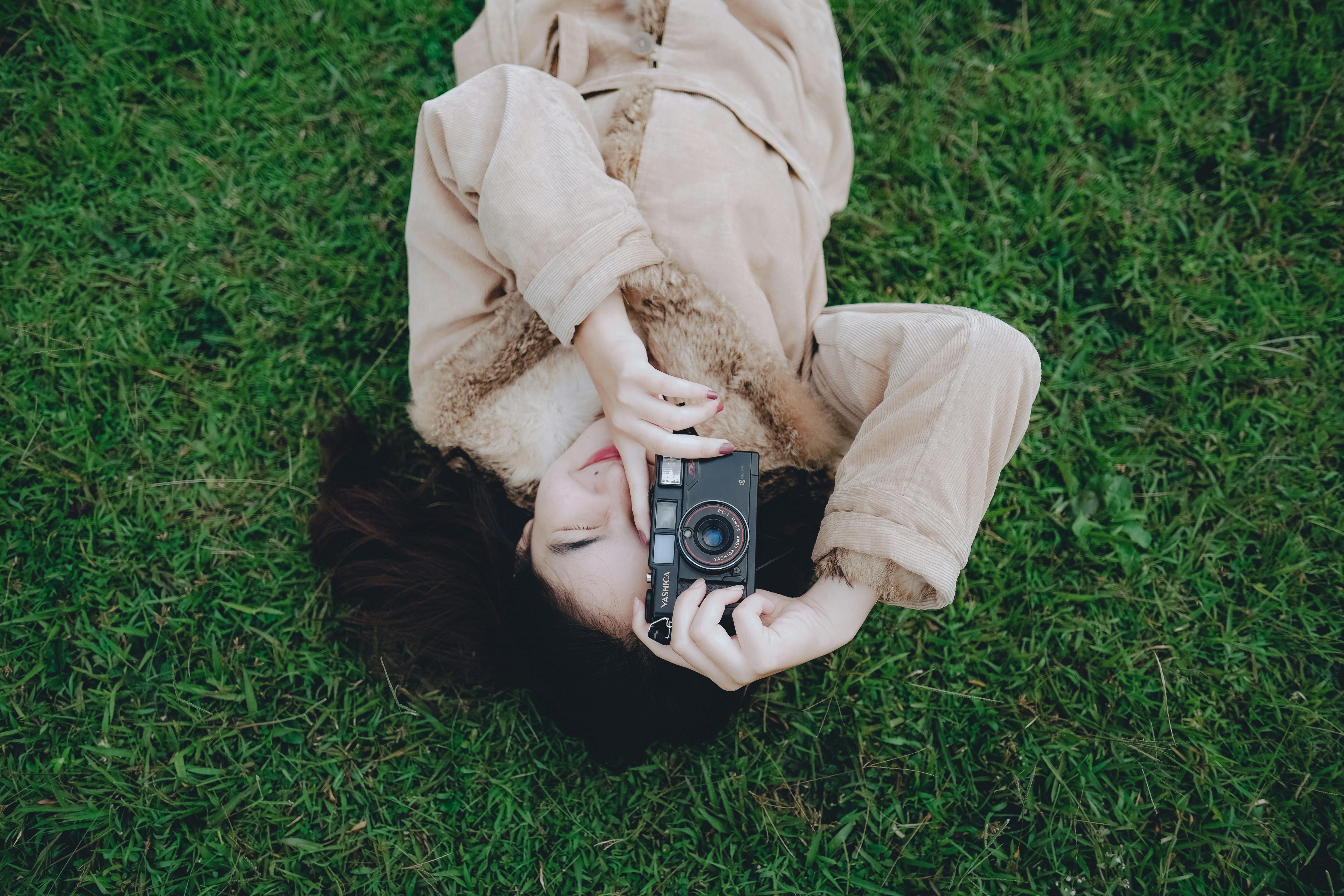 Asian woman lying in a grass field with DSLR, capturing moments.