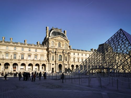 Free The Louvre Museum and Pyramid with tourists in Paris on a sunny day. Stock Photo