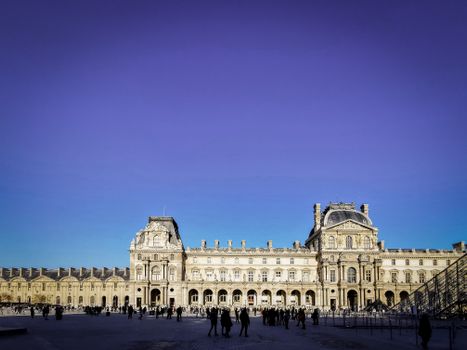 Louvre Museum in Paris with tourists, showcasing historic architecture under a clear blue sky.