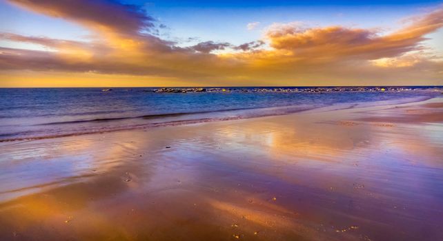 Stunning sunset on a serene beach with colorful reflections on the wet sand.