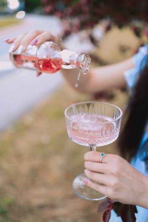 Person Pouring Pink Liquid on Clear Wine Glass
