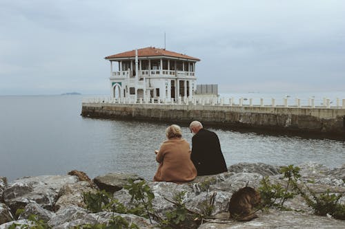 A Senior Couple Sitting on a Rock while Looking at the Ocean