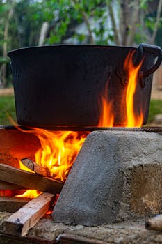A close-up view of a black cooking pot on a vibrant open fire outdoors, showcasing rustic outdoor cooking methods.