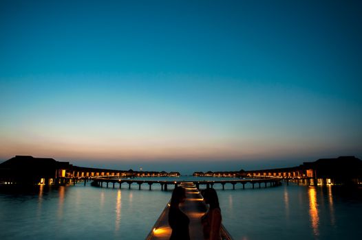Captivating sunset over illuminated overwater villas offering a serene and luxurious ambiance.