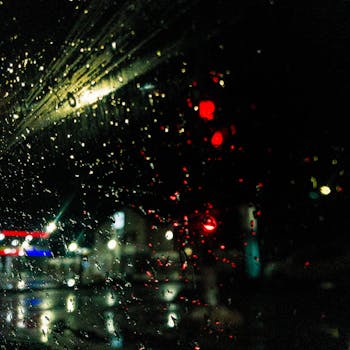 View of glowing city lights through rain-speckled window at night.