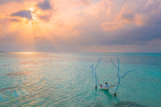 A couple relaxing in a hammock over the clear waters of Maldives at a gorgeous sunset.