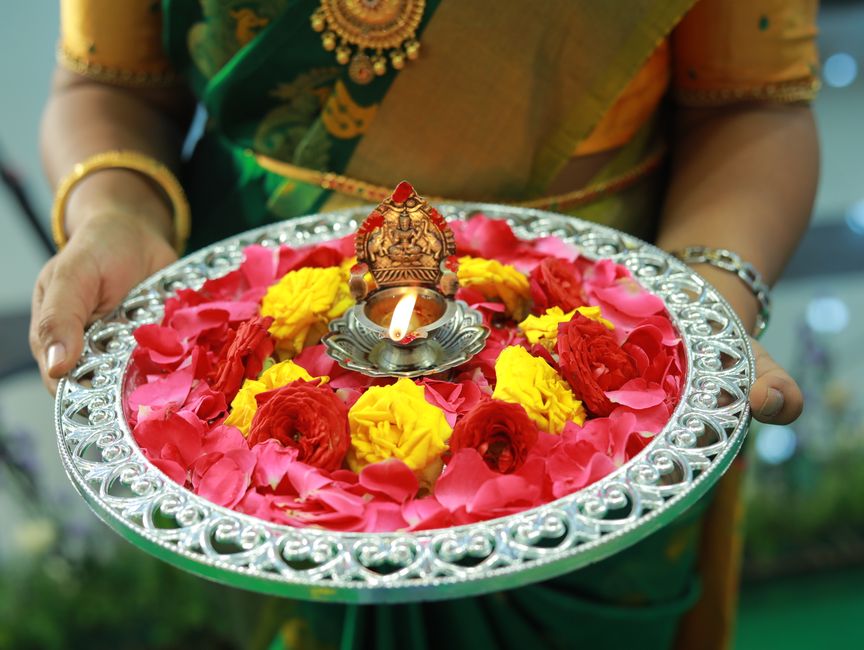 A vibrant Indian ceremony with a decorated plate of flowers and lit diya, symbolizing tradition.