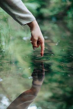 A hand gently touches a pond, creating ripples amidst a serene outdoor setting.