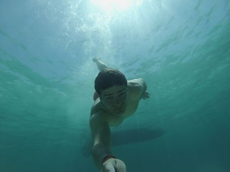 A young man swimming underwater in sunny, clear blue sea, capturing summer leisure.