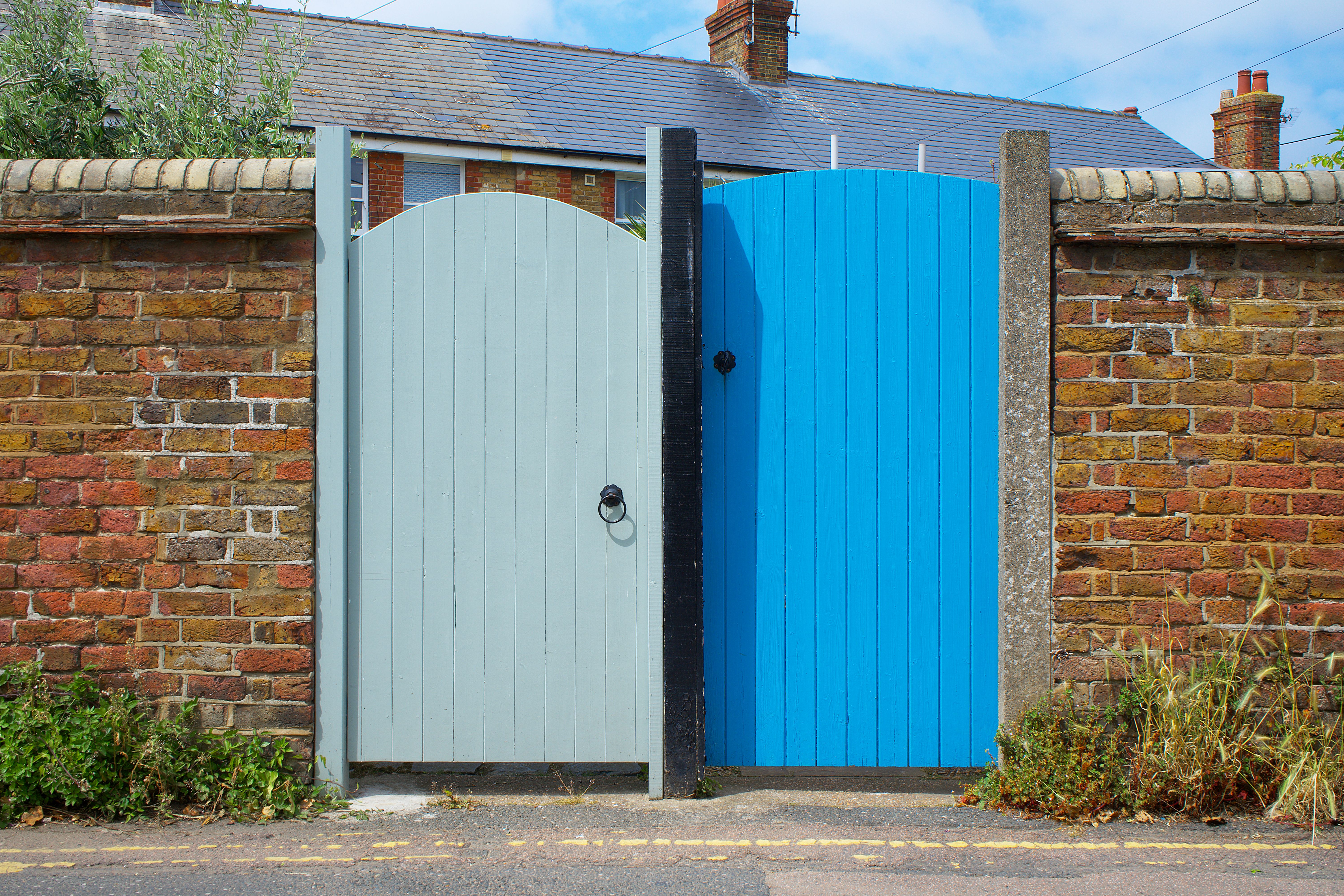 A vibrant blue gate set in a rustic brick wall on a sunny day in Whitstable, England.