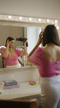Woman in pink top filming a vlog in front of a mirror, capturing her reflection.