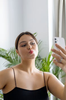 Young woman taking a selfie indoors with her smartphone, striking a playful pose.