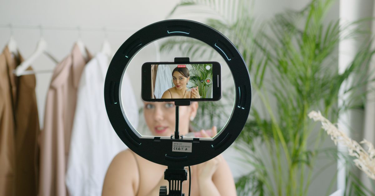 Woman creating video content using smartphone and ring light setup indoors.