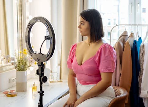 Young woman in pink top setting up camera for video recording with ring light indoors.