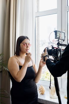 Young woman films a makeup tutorial at home with a professional DSLR camera setup.