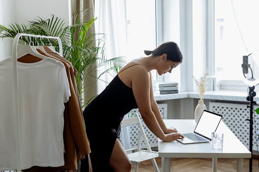 Businesswoman using laptop at home office desk with ring light and indoor plants.