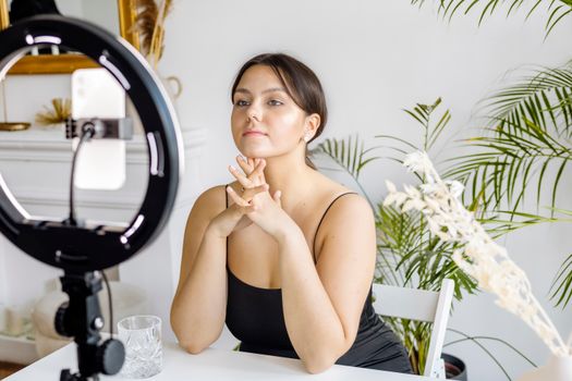 Young woman using ring light and cellphone for vlogging in a trendy, indoor setup with homeplants.