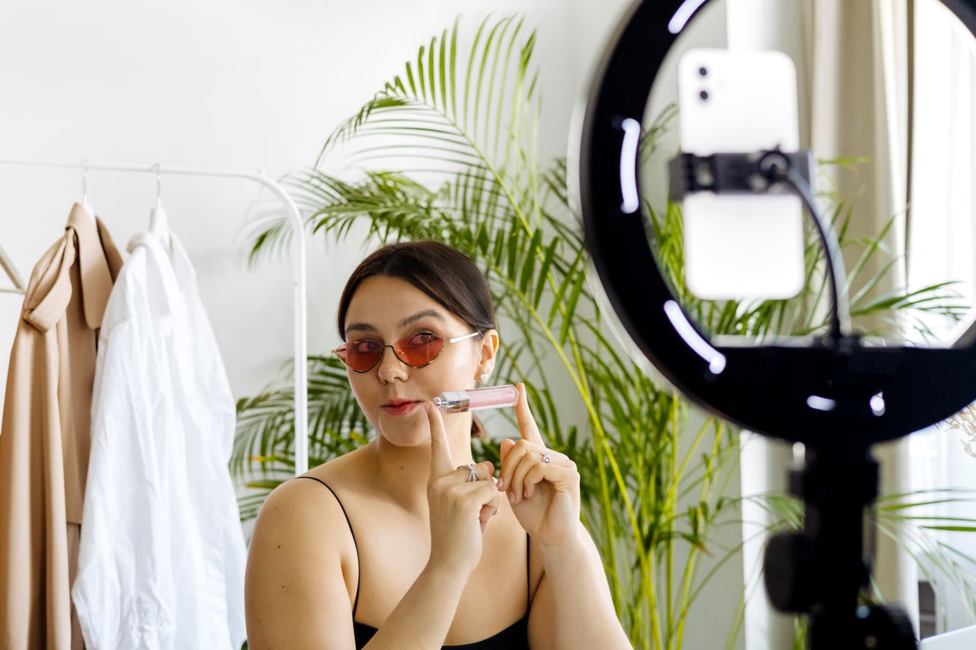 Content creator presenting a cosmetic product while filming with a smartphone and ring light