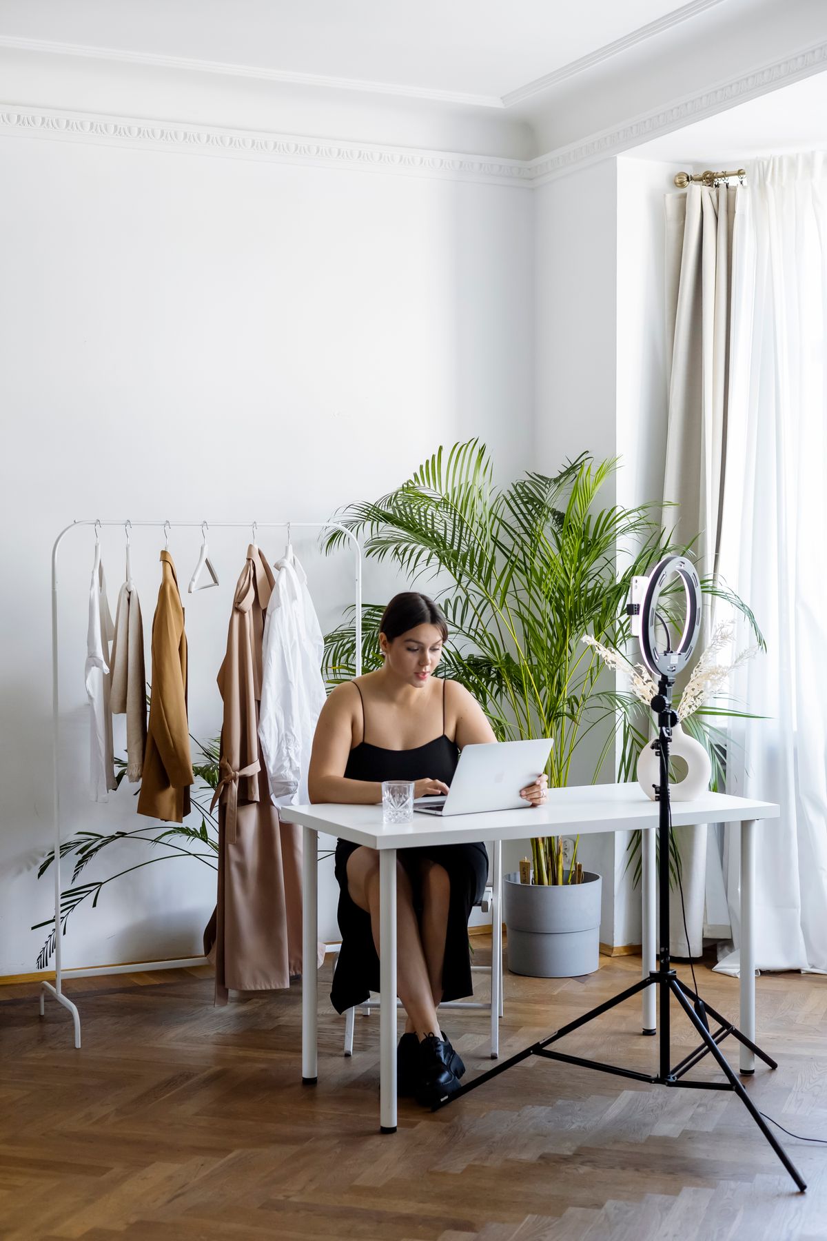 Content creator working at a laptop beside a ring light and clothing rack for online selling