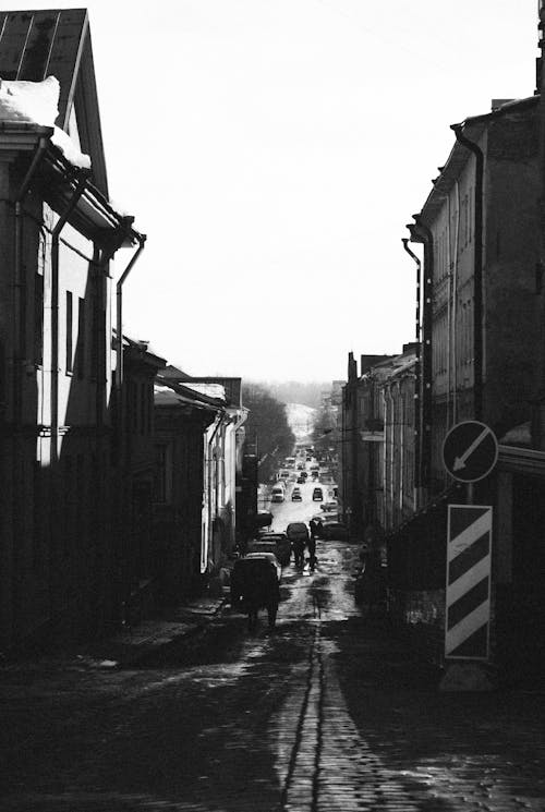 Grayscale Photo of People Walking on Street Between Buildings