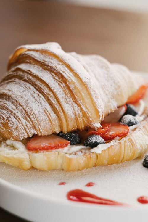 Free Close-up of flaky croissant filled with juicy berries and cream, dusted with sugar. Stock Photo