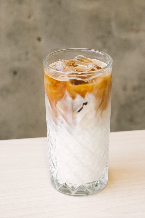 Free Chilled iced milk tea with a layered effect served in a textured glass on a neutral background. Stock Photo