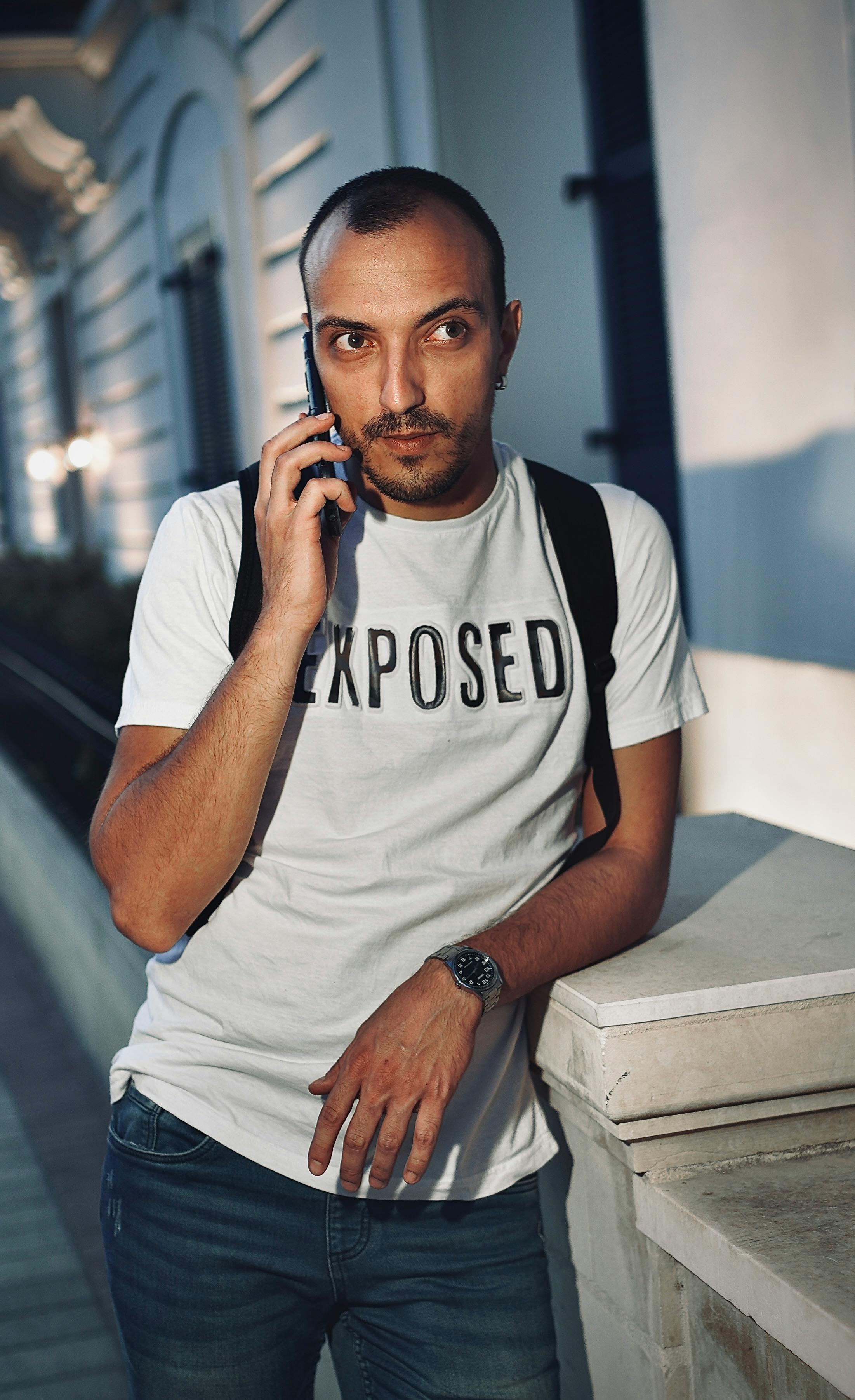 Casual adult man in Malta making a phone call at night, wearing a white t-shirt.