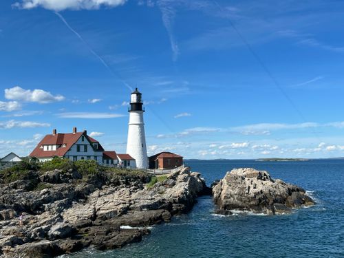 Free A picturesque lighthouse perched on rocky cliffs overlooking the ocean under a clear blue sky. Stock Photo
