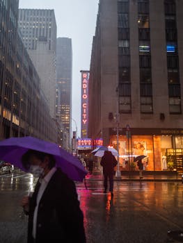 People with umbrellas walking past Radio City in New York on a rainy day.