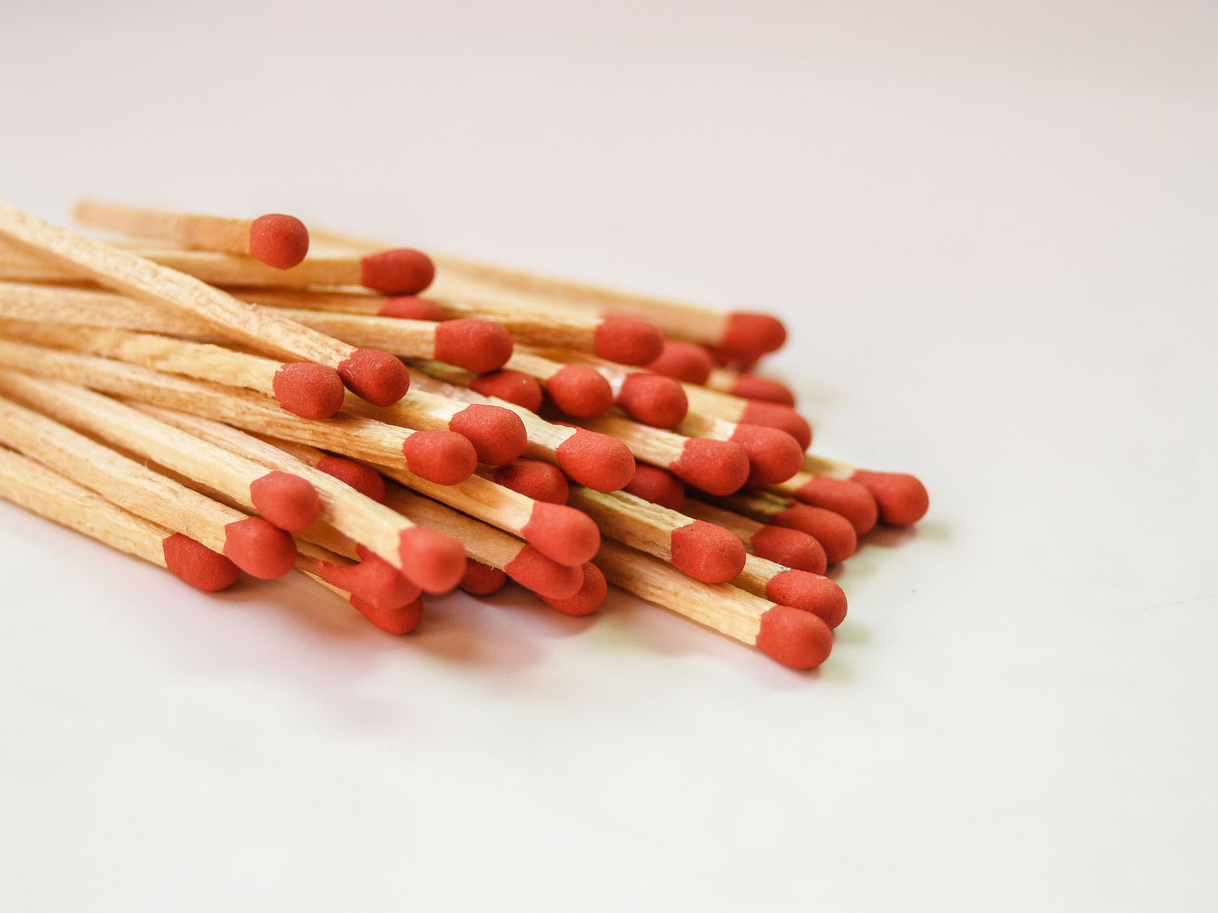 Close-up of a pile of wooden matches with red heads on a plain background.