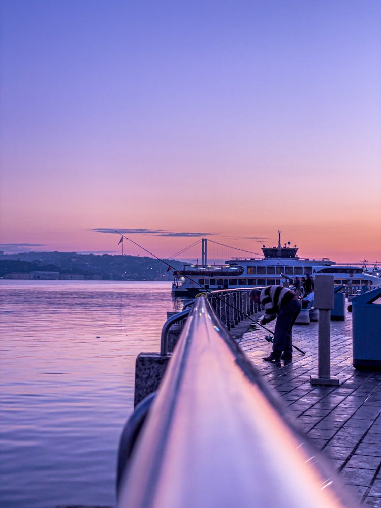 A Man Looking At The Fishing Rod While Standing On A Dock