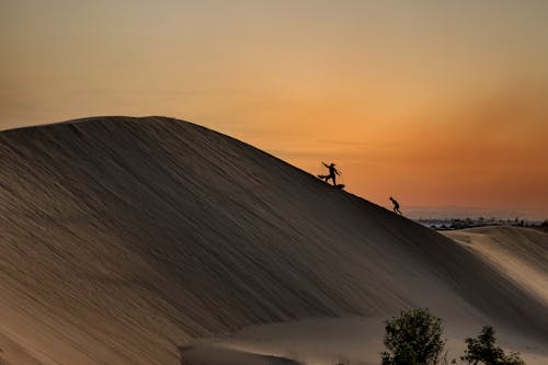 People Climbing Sand Dune at Sunset