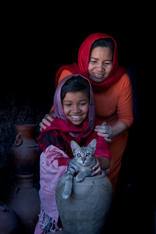 Mother and Daughter Wearing Headscarf Looking at the Gray Cat on the Jar