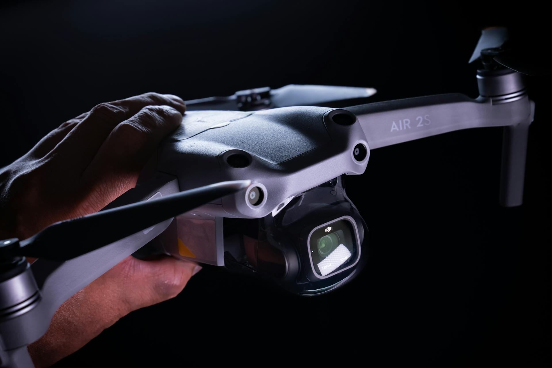 A close-up of a hand holding a DJI drone against a dark background, highlighting its camera.