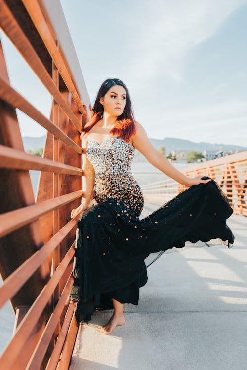 Woman in Glittery Black Dress Near Metal Railing